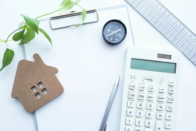 机の上に、計算機と時計、ペン、家のオブジェなどが置かれている