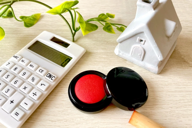 机の上に、家のオブジェと計算機、朱肉が置かれている