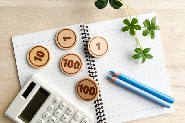 ノートと電卓、硬貨、鉛筆が机に並び、家事按分や経費管理の作業をイメージしている