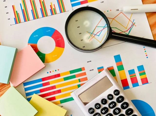 グラフが書かれたペーパーの上に虫眼鏡や計算機、付箋が散乱している