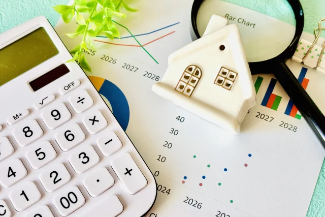 電卓とグラフ資料の上に家の模型が置かれ、住宅ローン控除や利息計算のイメージになっている