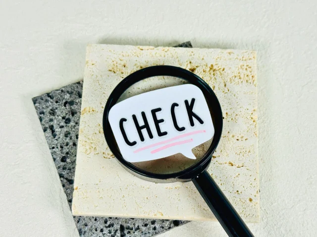 石のタイル2枚の上に、虫眼鏡が置かれ、そのレンズ部分に「CHECK」と書かれた吹き出しが置かれている