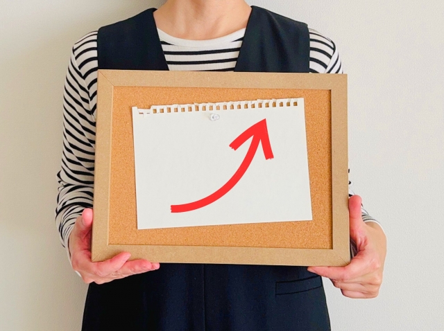 右上へ向けて伸びる矢印が書かれた紙片を貼り付けたコルクボードを持つ人。